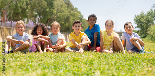 Group of happy kids friends resting on grass together in park at summer day