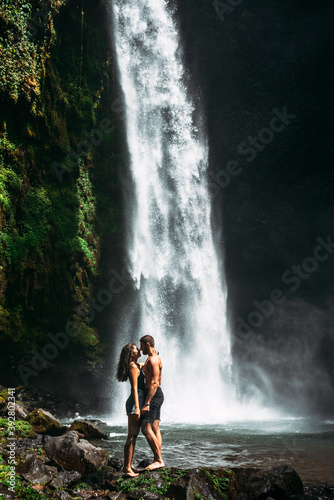 Beautiful couple at a waterfall in Indonesia. A couple in love travels around the island of Bali. A man and a woman kiss at the waterfall. Travel to Asia. Honeymoon trip. Tourists at the waterfall