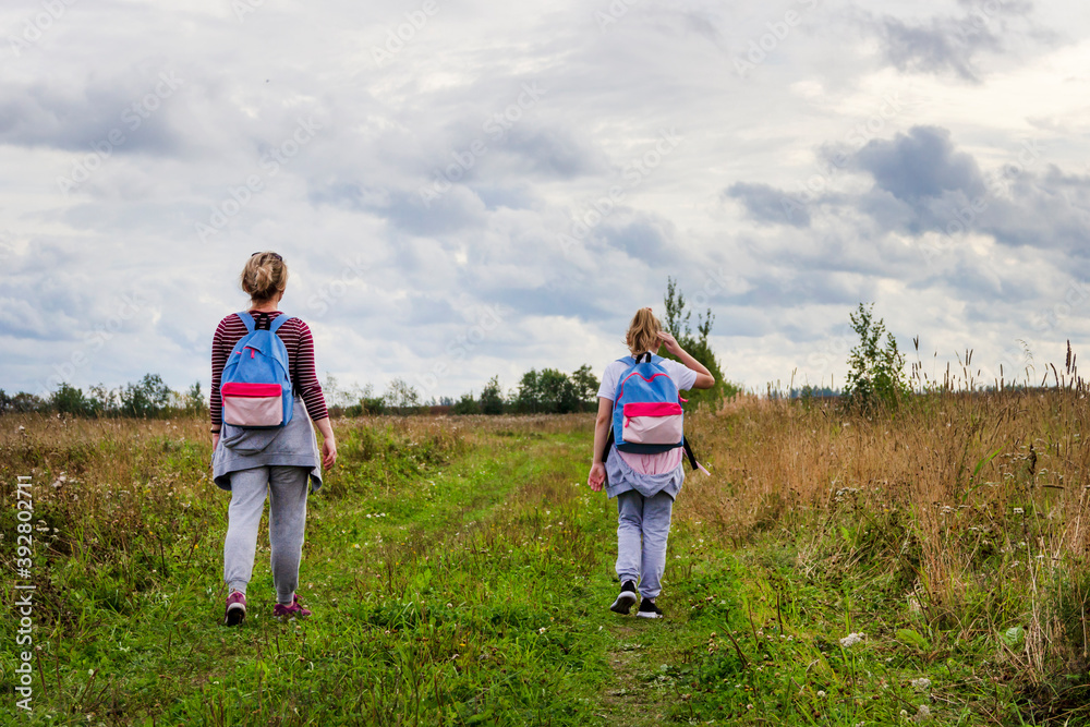 A mother and daughter walk along a road that goes far into the field, in early autumn, against the background of a sky with thick clouds. A mother and daughter walk along a road that goes far into the field, in early autumn, against the background of a sky with thick clouds.