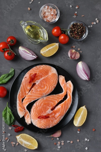 Fresh raw salmon steaks on a grill pan and ingredients on a dark background. Top view. Vertical format