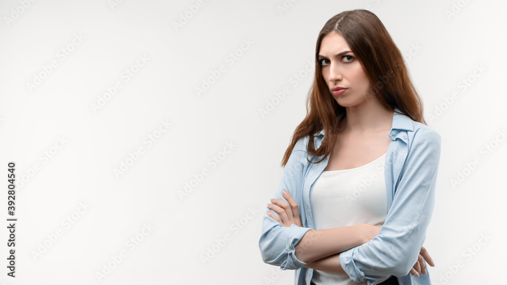 Displeased brunette female stands with her arms crossed, dressed in casual clothes. Copy space. Isolated on white Displeased brunette female stands with her arms crossed, dressed in casual clothes. Copy space. Isolated on white