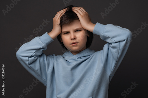 Image of stressed boy 10-12 years old grabbing his head. Emotional helplessness. Studio shot, gray background