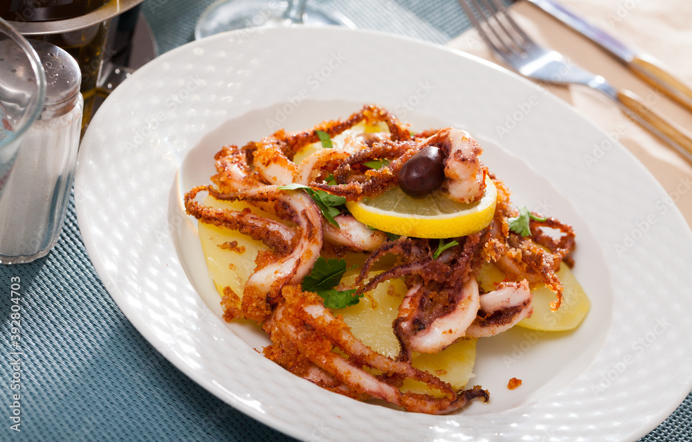 Fried spicy tentacles squid served on white plate with potatoes, lemon slices and fresh parsley