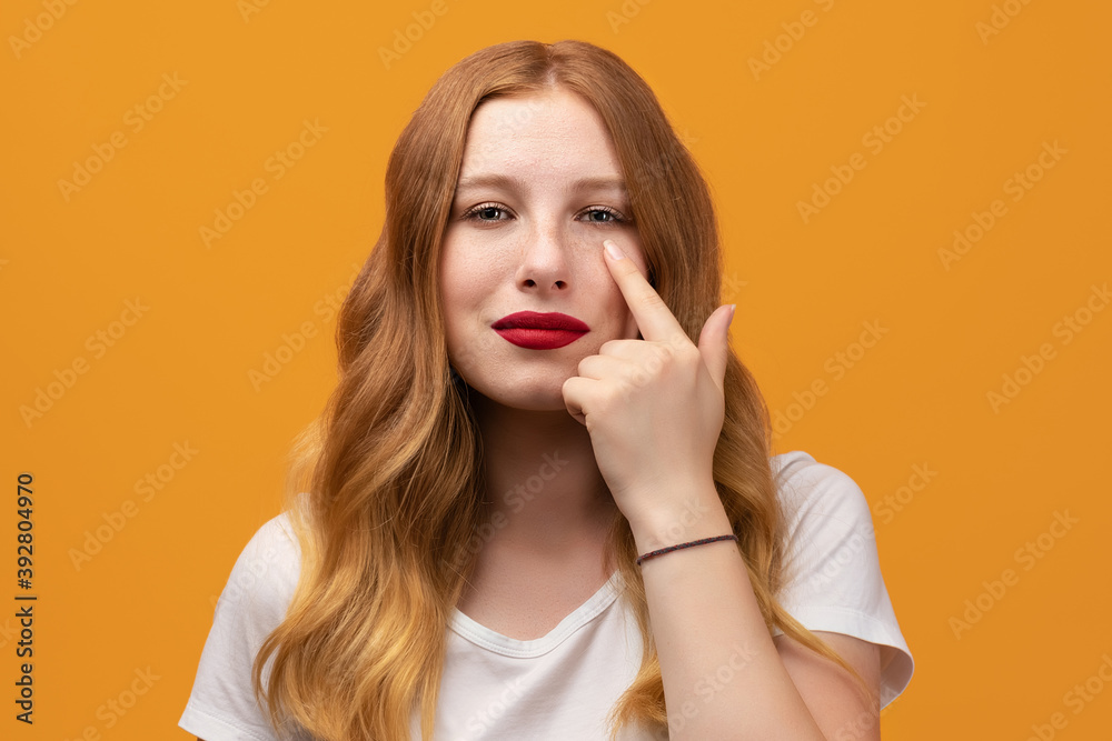 Pretty girl with wavy redhead pointing to the eye watching you gesture, suspicious expression Pretty girl with wavy redhead pointing to the eye watching you gesture, suspicious expression