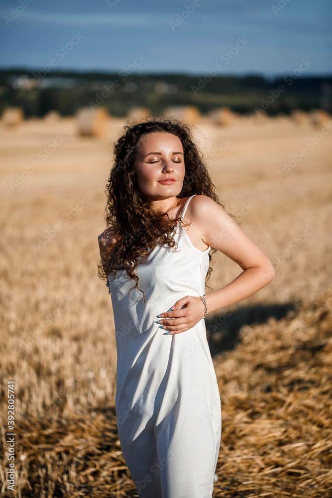 Portrait of a young curly woman in a wheat field, where the wheat is mown and the sheaves are standing, enjoying nature. Nature. sun rays Agriculture Portrait of a young curly woman in a wheat field, where the wheat is mown and the sheaves are standing, enjoying nature. Nature. sun rays Agriculture