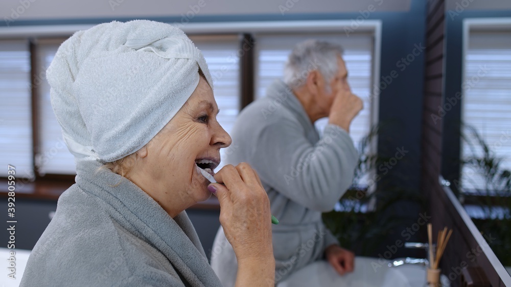 Attractive loving old senior couple man and woman brushing teeth and looking into a mirror. Cheerful elderly grandmother and grandfather doing morning hygiene at luxury bathroom at home Attractive loving old senior couple man and woman brushing teeth and looking into a mirror. Cheerful elderly grandmother and grandfather doing morning hygiene at luxury bathroom at home