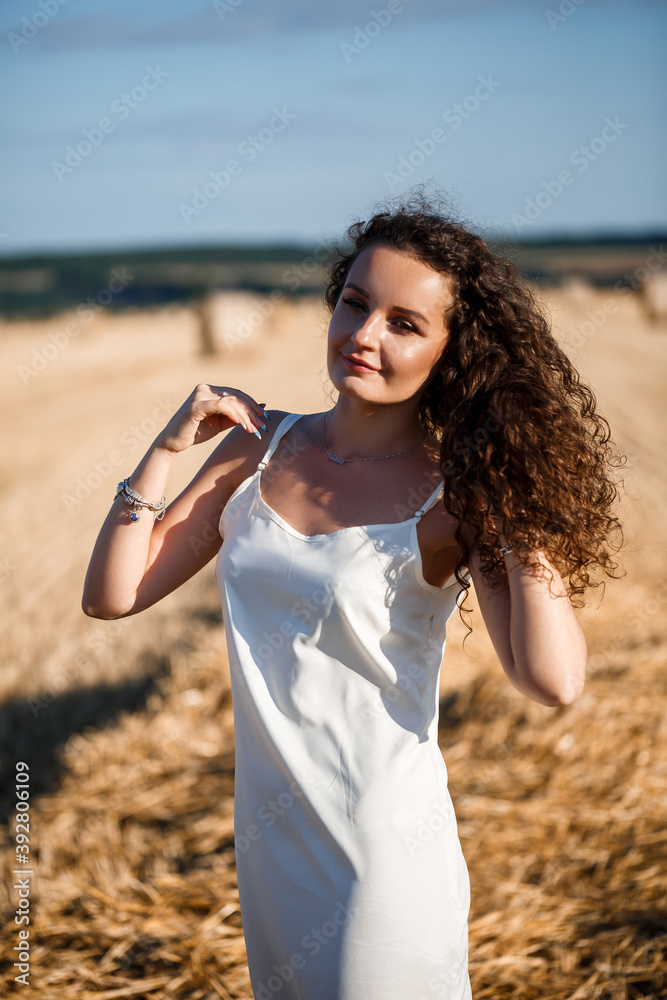 Portrait of a young curly woman in a wheat field, where the wheat is mown and the sheaves are standing, enjoying nature. Nature. sun rays Agriculture