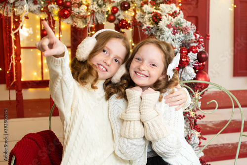two red-haired sisters on the veranda of a house decorated for Christmas. to point with a finger.