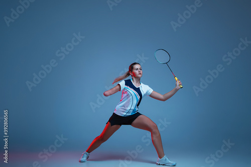 On the run. Beautiful handicap woman practicing in badminton isolated on blue background in neon light. Lifestyle of inclusive people, diversity and equility. Sport, activity and movement. Copyspace.