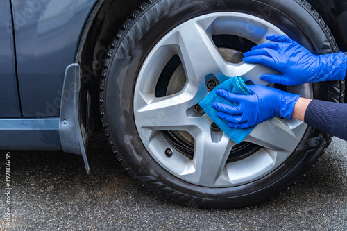 Hands dressed in rubber blue gloves clean the wheel of the car with a blue microfiber cloth.