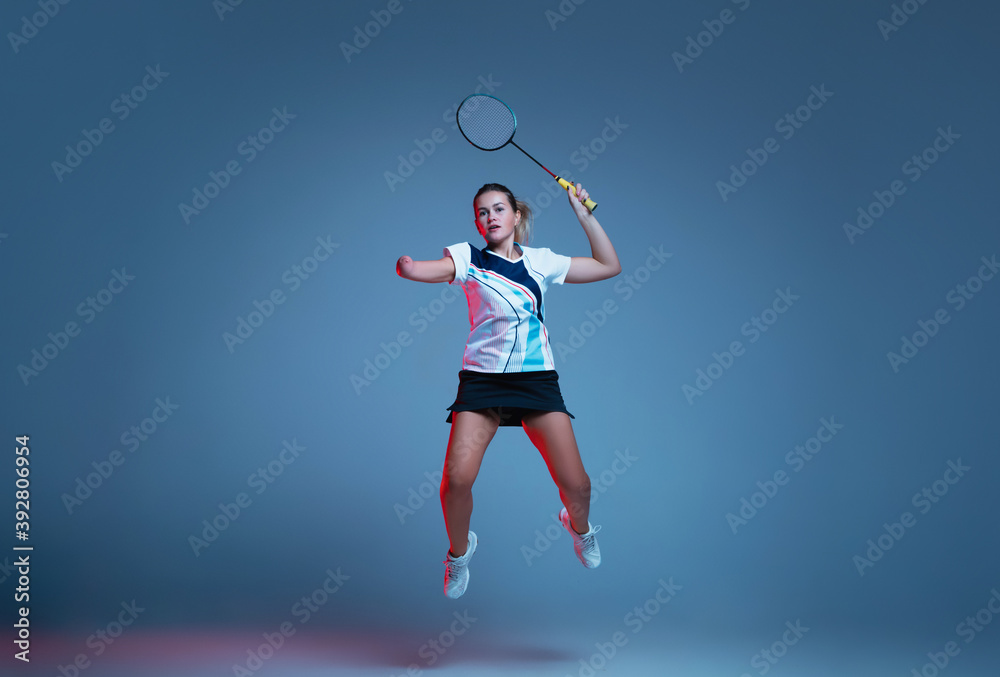 On the run. Beautiful handicap woman practicing in badminton isolated on blue background in neon light. Lifestyle of inclusive people, diversity and equility. Sport, activity and movement. Copyspace. On the run. Beautiful handicap woman practicing in badminton isolated on blue background in neon light. Lifestyle of inclusive people, diversity and equility. Sport, activity and movement. Copyspace.