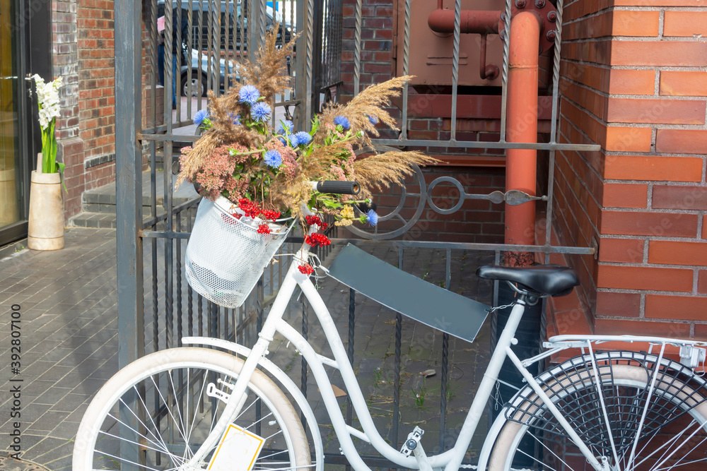 White bike with a basket of wildflowers on a city street. Copy space, selective focus