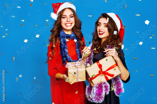 Christmas young women. Smiling women in santa claus hat holding many gift boxes. Winter holiday.