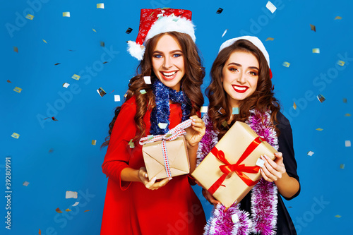 Christmas young women. Smiling women in santa claus hat holding many gift boxes. Winter holiday.