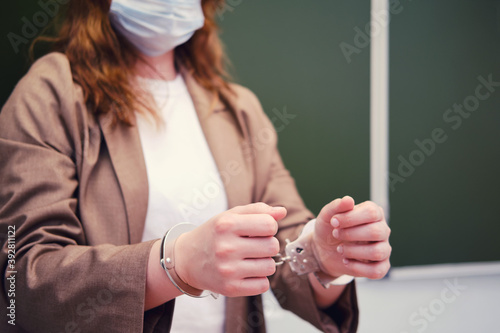 Woman teacher in handcuffs stands at the blackboard, concept of problems with coronavirus. The problem with lessons in the classroom during the virus outbreak