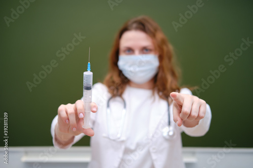 Doctor with a large vaccination syringe points his finger at you. Learning difficulties in the flu pandemic