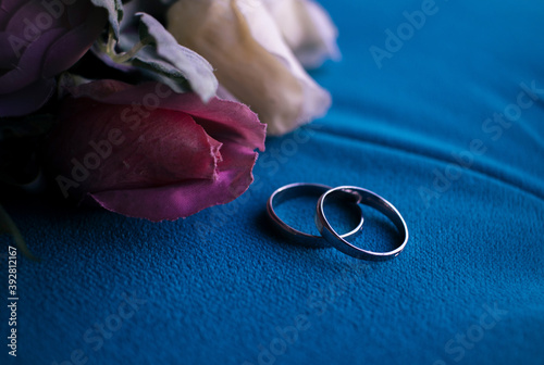 photo of wedding rings with flowers on blue fabric close up