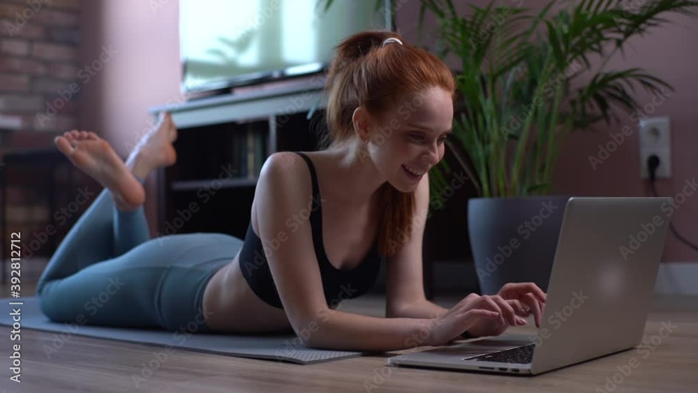 Portrait of cheerful young woman lying on the floor and using laptop computer at apartment. Sporty smiling female having online chatting via notebook while resting after sport training. Portrait of cheerful young woman lying on the floor and using laptop computer at apartment. Sporty smiling female having online chatting via notebook while resting after sport training.