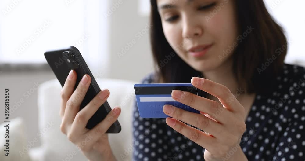 Close up focus on cellphone and plastic bank card, smiling female asian korean client entering payment information in shopping application, purchasing goods or services quickly in online store. Close up focus on cellphone and plastic bank card, smiling female asian korean client entering payment information in shopping application, purchasing goods or services quickly in online store.