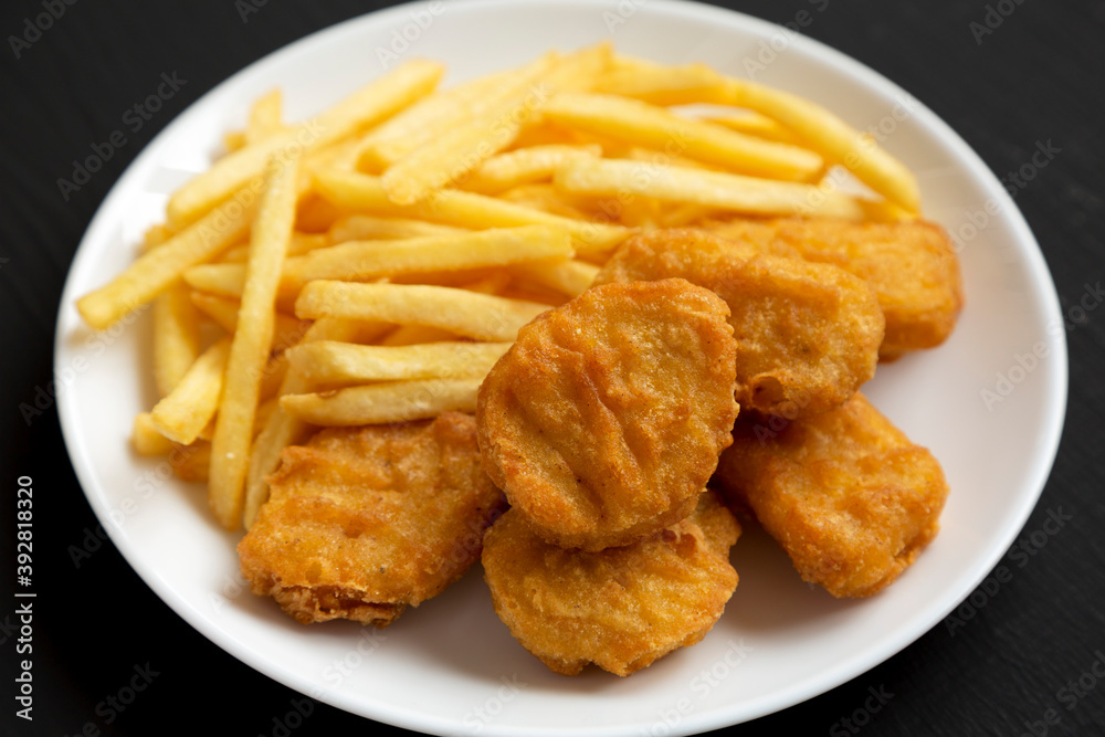 Tasty Fastfood: Chicken Nuggets and French Fries on a plate on a black background, side view. Tasty Fastfood: Chicken Nuggets and French Fries on a plate on a black background, side view.