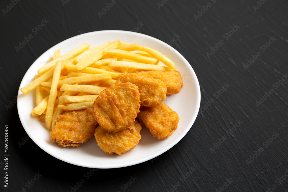 Tasty Fastfood: Chicken Nuggets and French Fries on a plate on a black surface, side view. Copy space. Tasty Fastfood: Chicken Nuggets and French Fries on a plate on a black surface, side view. Copy space.