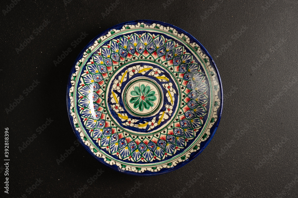 Ethnic Uzbek ceramic tableware on the black background. Decorative ceramic plate.