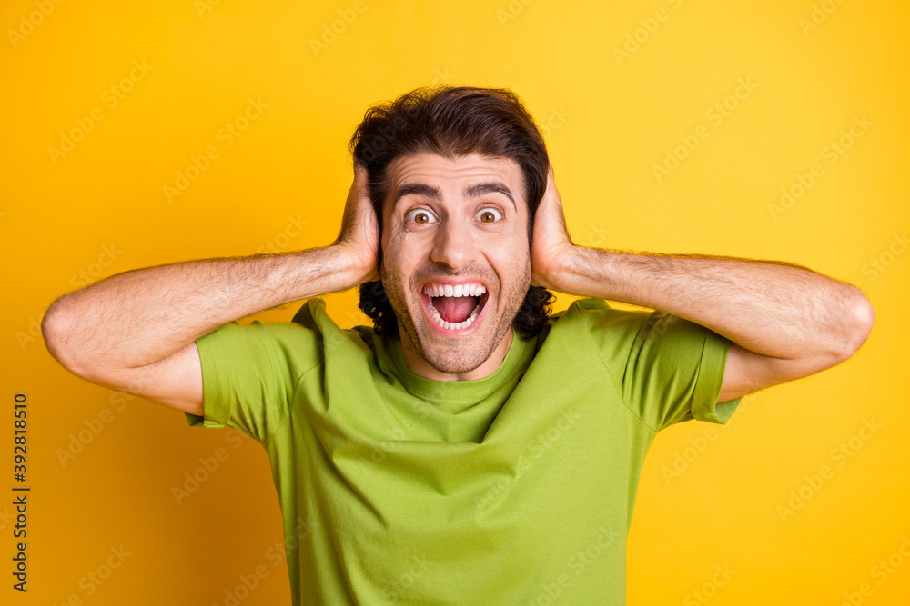 Photo of excited crazy man hands cover ears open mouth wear green t-shirt isolated yellow color background Photo of excited crazy man hands cover ears open mouth wear green t-shirt isolated yellow color background