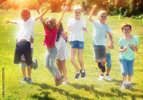 Happy team of friends children jumping together in park outdoors