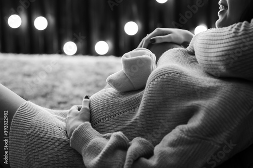 Obraz na płótnie Black and white cropped image of beautiful happy pregnant woman and her husband holding baby shoes and hugging the tummy. w salonie