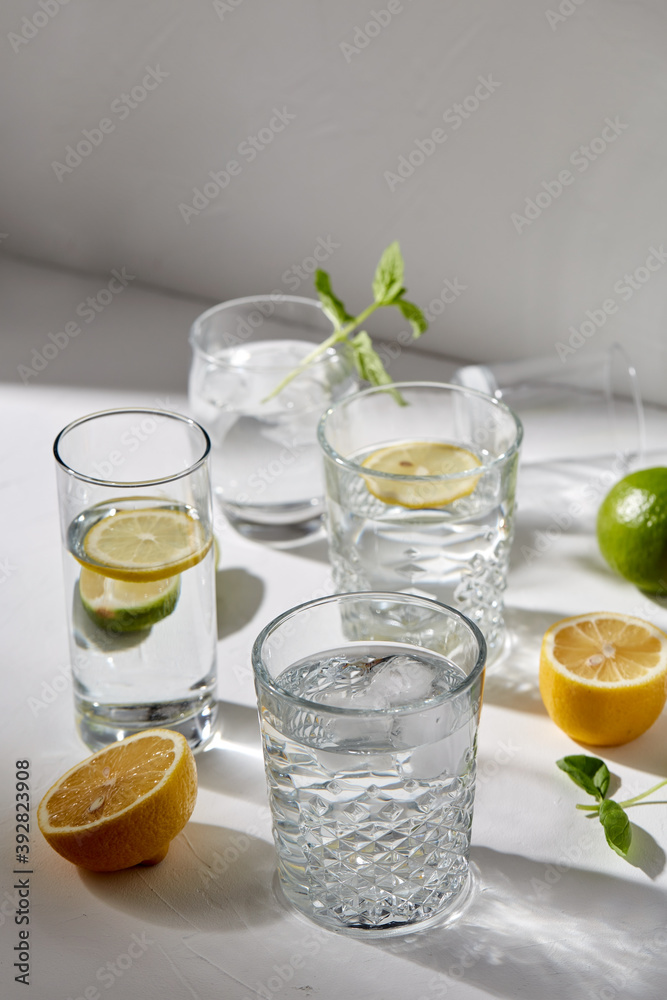 drink, detox and diet concept - glasses with fruit water or lemonade, lemons, limes and peppermint on white table drink, detox and diet concept - glasses with fruit water or lemonade, lemons, limes and peppermint on white table