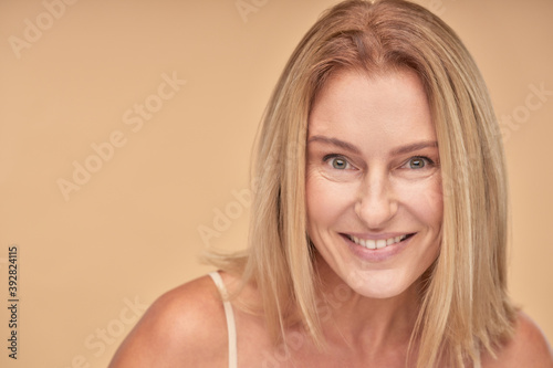 Portrait of beautiful mature woman smiling at camera while posing in studio over beige background