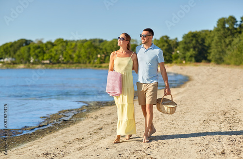 leisure, relationships and people concept - happy couple with picnic basket walking along beach
