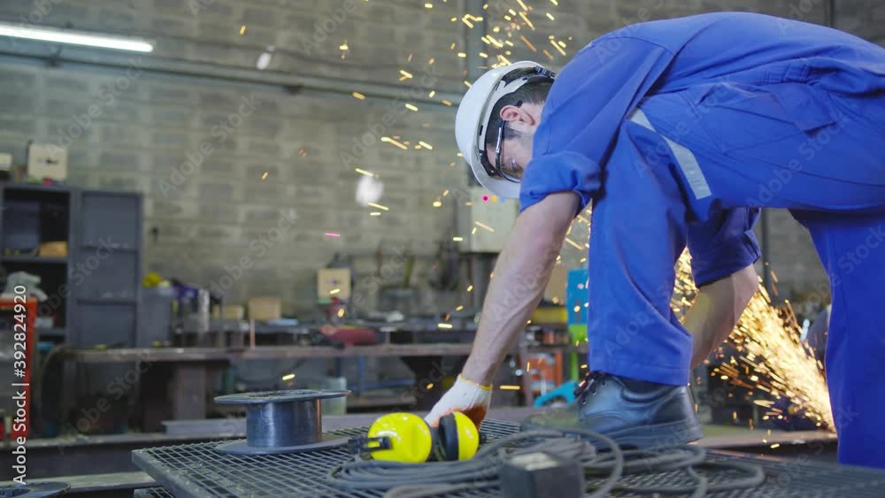 Caucasian male worker in a safty uniform wear welders leathers,qc cheching and measurement with Electric wheel grinding on steel structure in factor in the garage, orange bokeh sparks fly to the sides Caucasian male worker in a safty uniform wear welders leathers,qc cheching and measurement with Electric wheel grinding on steel structure in factor in the garage, orange bokeh sparks fly to the sides