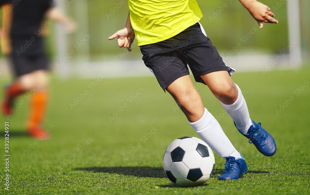 Young boy in yellow soccer jersey uniform running after ball on training pitch. Kid improving dribbling skills on practice session