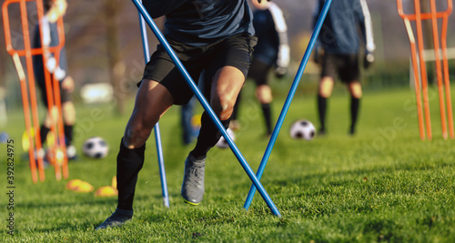 African-American soccer player on training drill. Legs of footballer running on grass practice field. Obstacle course in soccer football. Player running in sports cleats © matimix