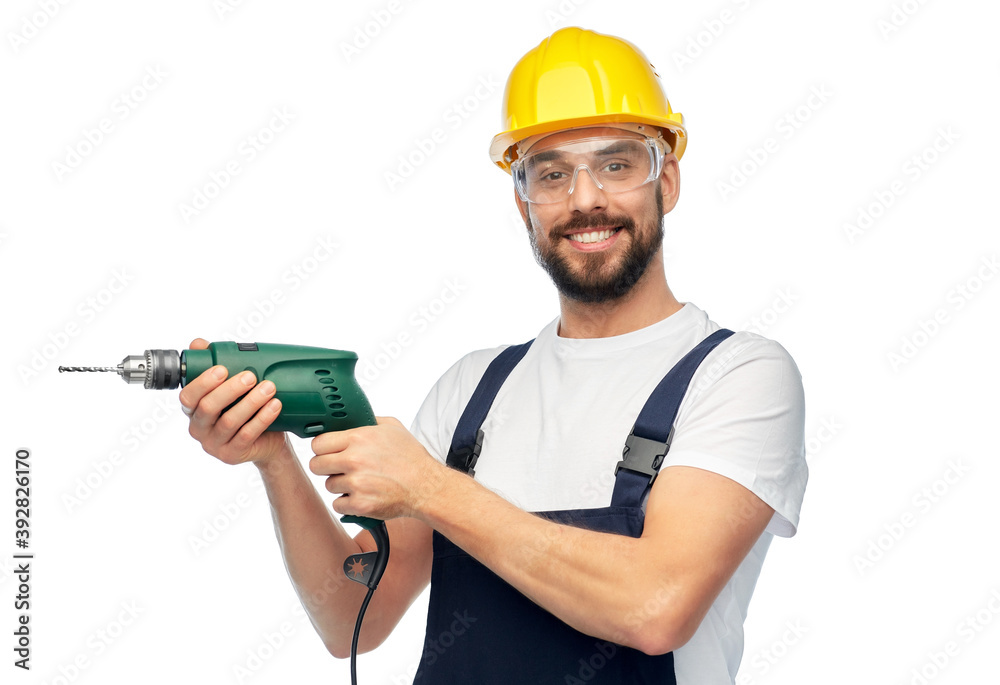 profession, construction and building - happy smiling male worker or builder in helmet and goggles with drill over white background