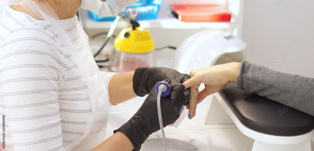 a woman of European appearance, with blond hair, in a protective medical mask, makes a professional manicure to a client, in a beauty salon. Beauty treatments during a pandemic a woman of European appearance, with blond hair, in a protective medical mask, makes a professional manicure to a client, in a beauty salon. Beauty treatments during a pandemic