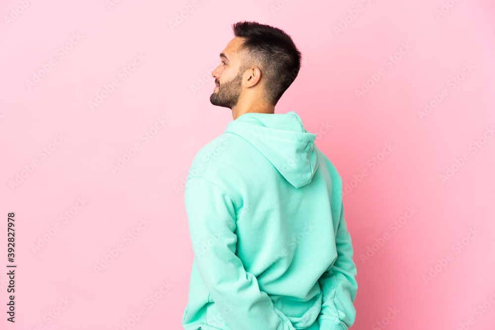 Young caucasian man isolated on pink background in back position and looking back Young caucasian man isolated on pink background in back position and looking back