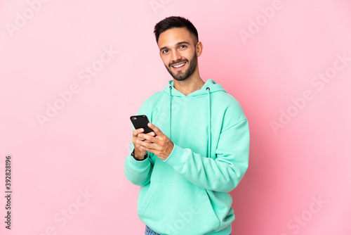 Young caucasian man isolated on pink background sending a message with the mobile