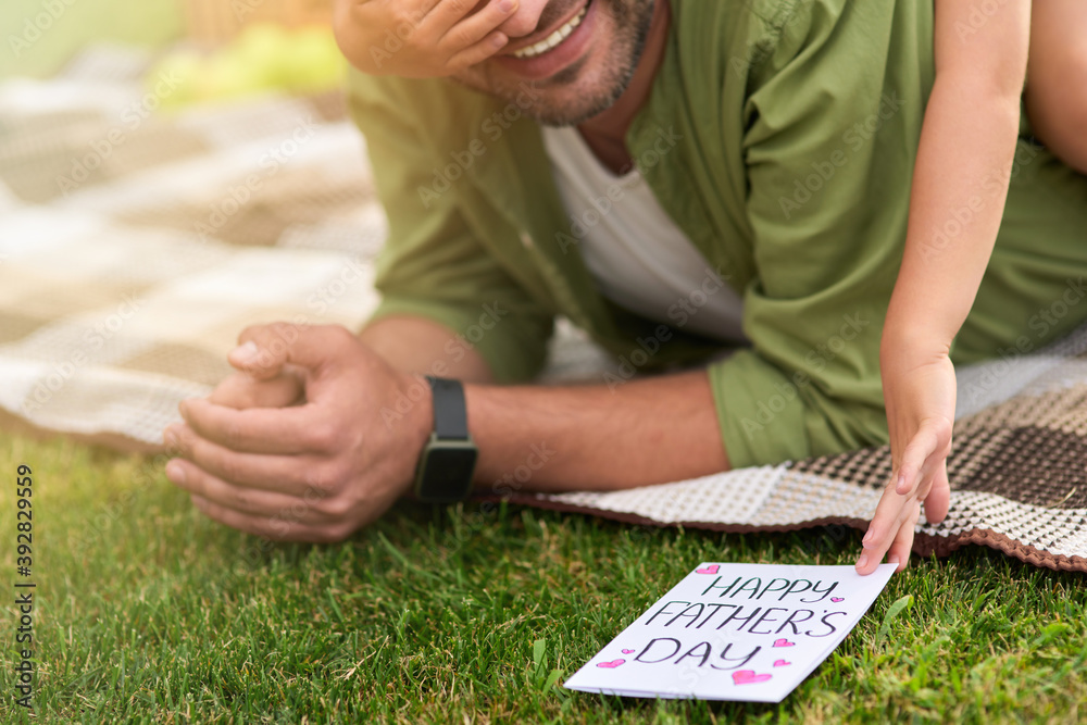 Cropped shot of little girl surprising her father, greeting and giving him handmade postcard, daddy and daughter celebrating Father's Day in the park Cropped shot of little girl surprising her father, greeting and giving him handmade postcard, daddy and daughter celebrating Father's Day in the park
