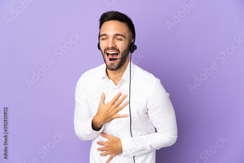 Telemarketer man working with a headset isolated on purple background smiling a lot