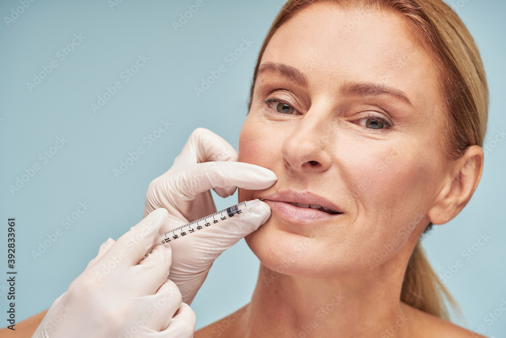 Beautiful mature caucasian woman making lip augmentation procedure by cosmetologist Beautiful mature caucasian woman making lip augmentation procedure by cosmetologist