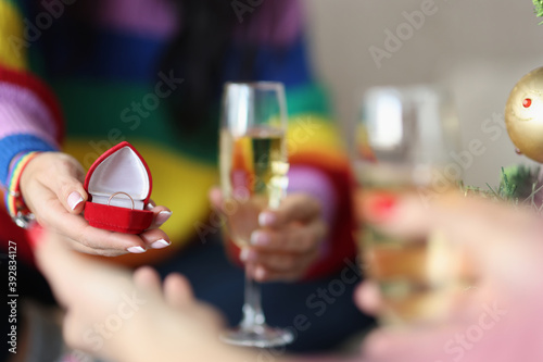 Woman's hand holds box with a wedding ring and a glass of champagne. Hand and heart proposals in gay families concept