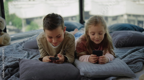 Tricky kids addicting mobile games. Siblings playing on smartphones at home.