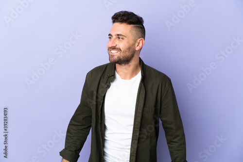 Caucasian man isolated on purple background looking to the side and smiling