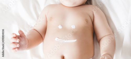 Smile sign on a baby s belly painted with a cream. baby lying on a white blanket. no face visible