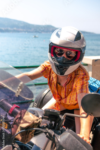 Young girl posing. Motorcycle for tourism and travel. Wearing a helmet. In the background are views of the sea and hotels. Coast of Italy. Sunny day, vacation and trip. Vertical photo © Sergey