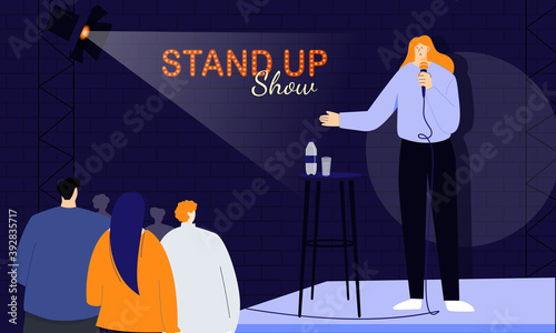 Young female stand-up comedian greets her audience at the beginning of the show, speaking directly to people through a microphone. Monologuing of humorous stories, jokes and one-liners.