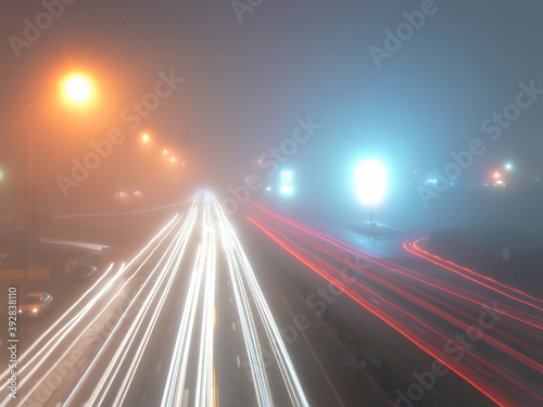 View of the night street in the fog with the burning street lamps and motorway tracks