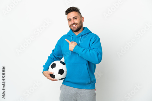 Caucasian man isolated on white background with soccer ball and pointing to the lateral